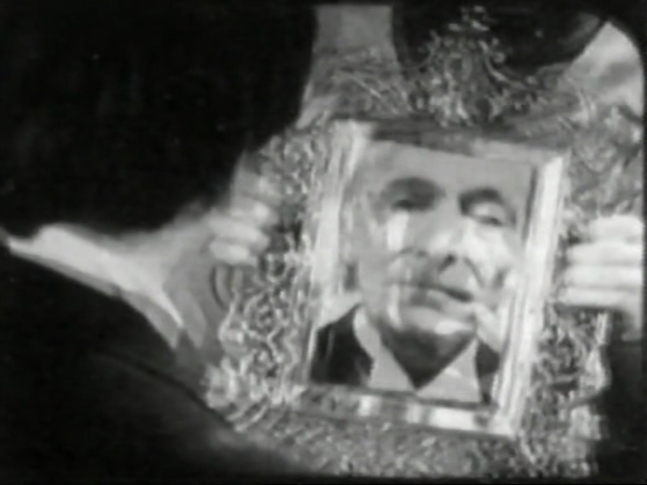 The Second Doctor looks into a mirror. The face reflected is that of the First Doctor.