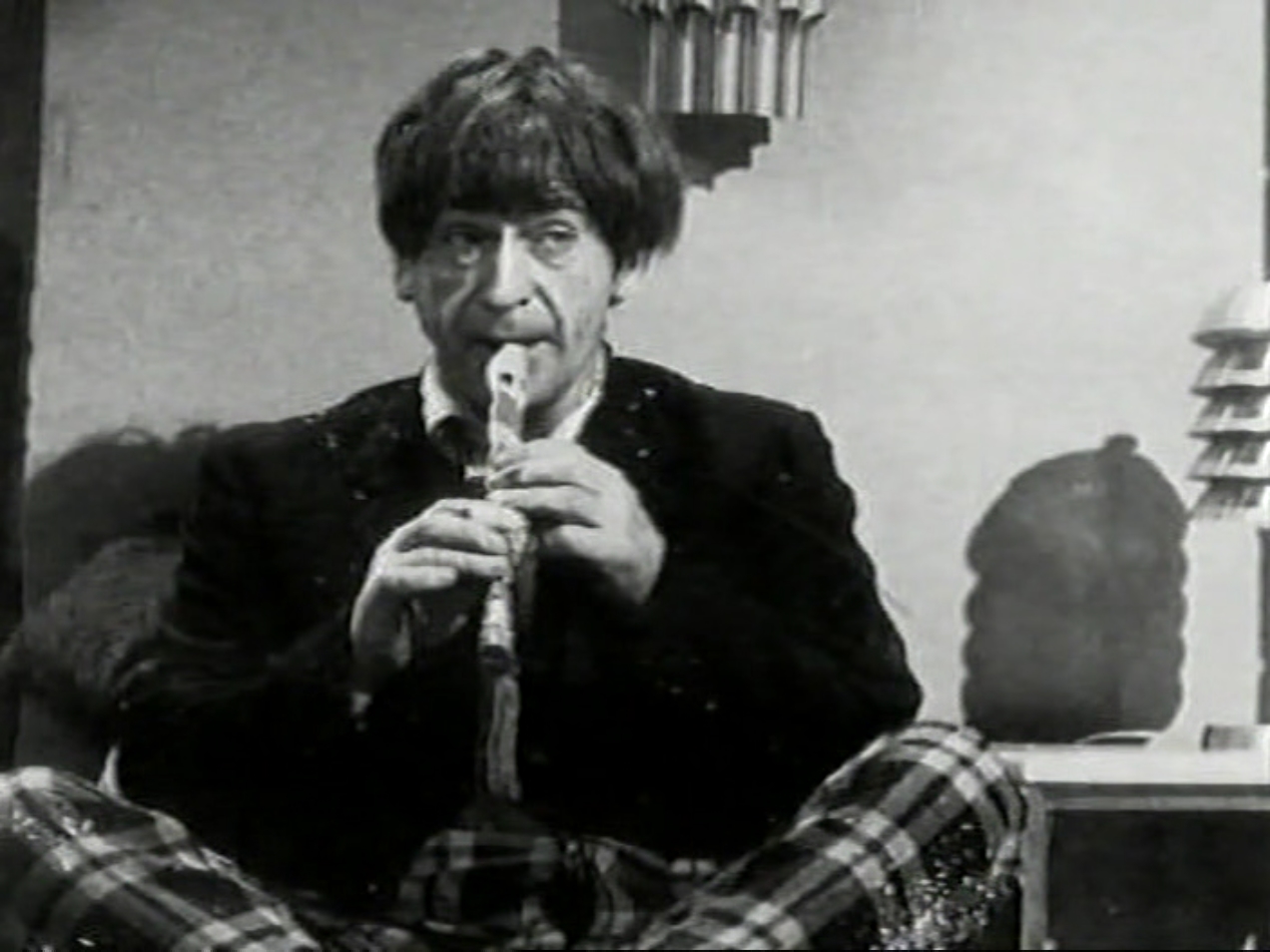 The Doctor sits cross-legged, playing a recorder.