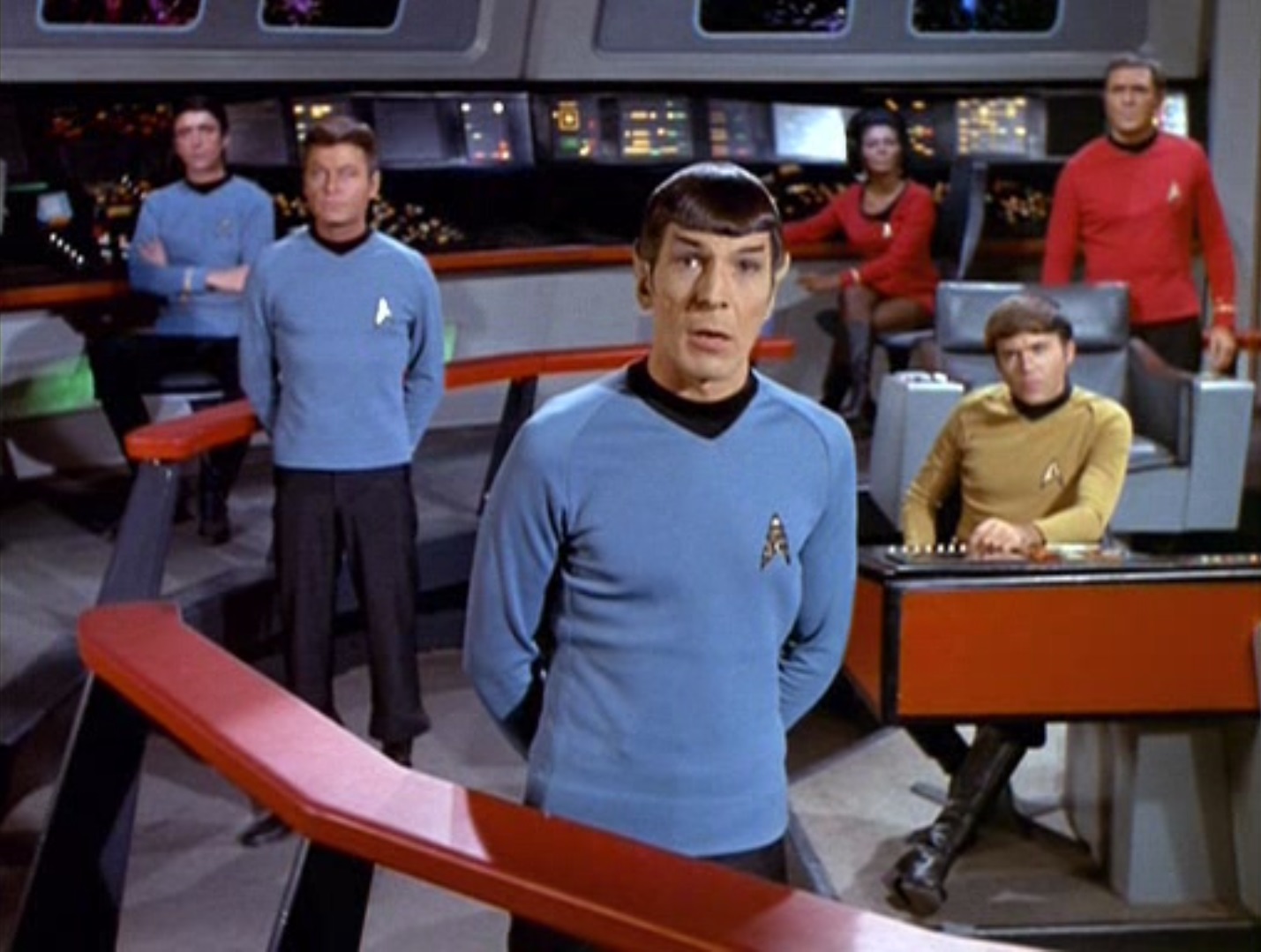 A beautifully staged shot of, from left to right, Lieutenant Brent, Dr. McCoy, Mr. Spock, Lieutenant Uhura, Ensign Chekov, and Mr. Scott, on the bridge of the Enterprise, as Spock parlays with Hodin