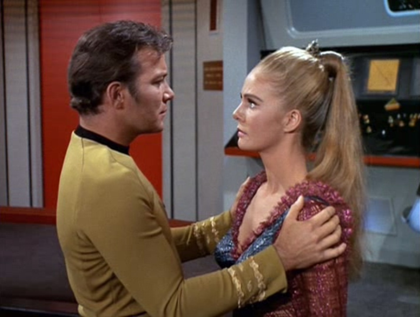 Kirk grips Odona by her shoulders passionately on the empty bridge of the fake Enterprise