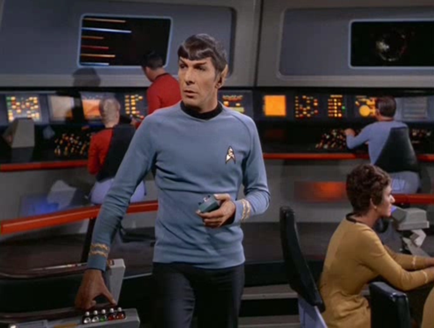 Spock gets up from his chair on the bridge, holding an gadget, several crewmembers behind him