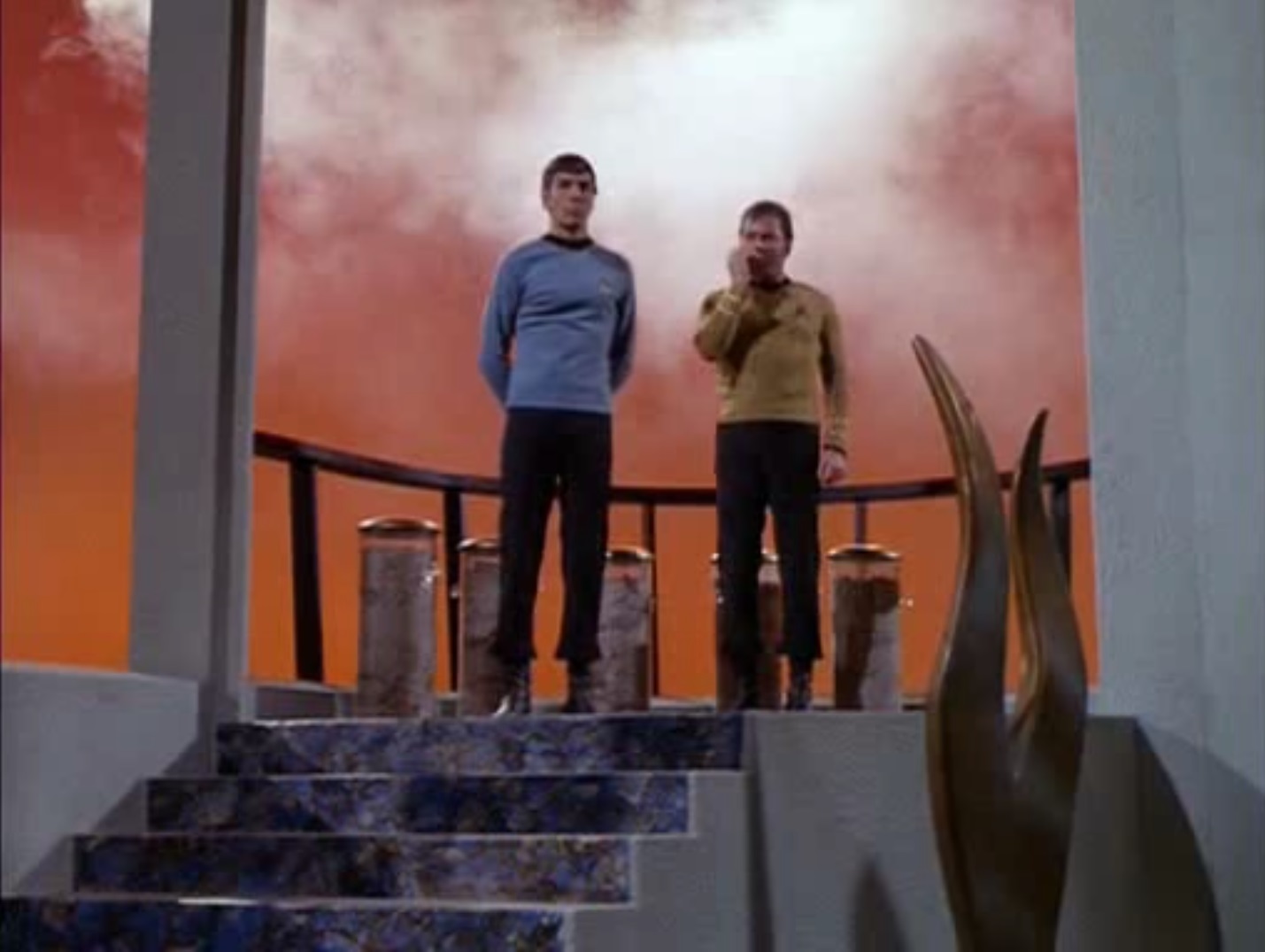 screen capture of Spock and Kirk on the transporter platform of the sky city, Stratos, Kirk holding a communicator to his mouth