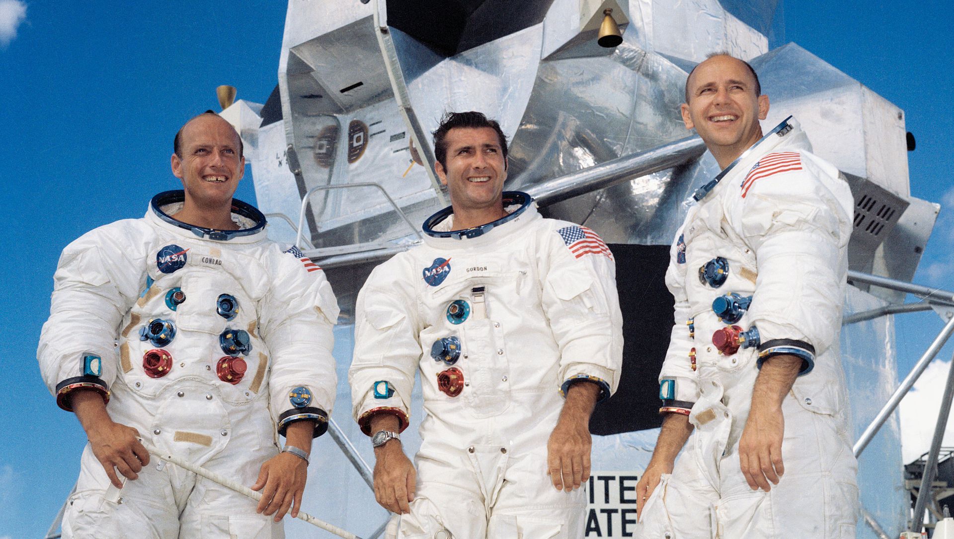 A promotional color photograph of astronauts Conrad, Gordon and Bean, in their spacesuits minus gloves and helmets, in front of the Apollo 12 Lunar Module. 