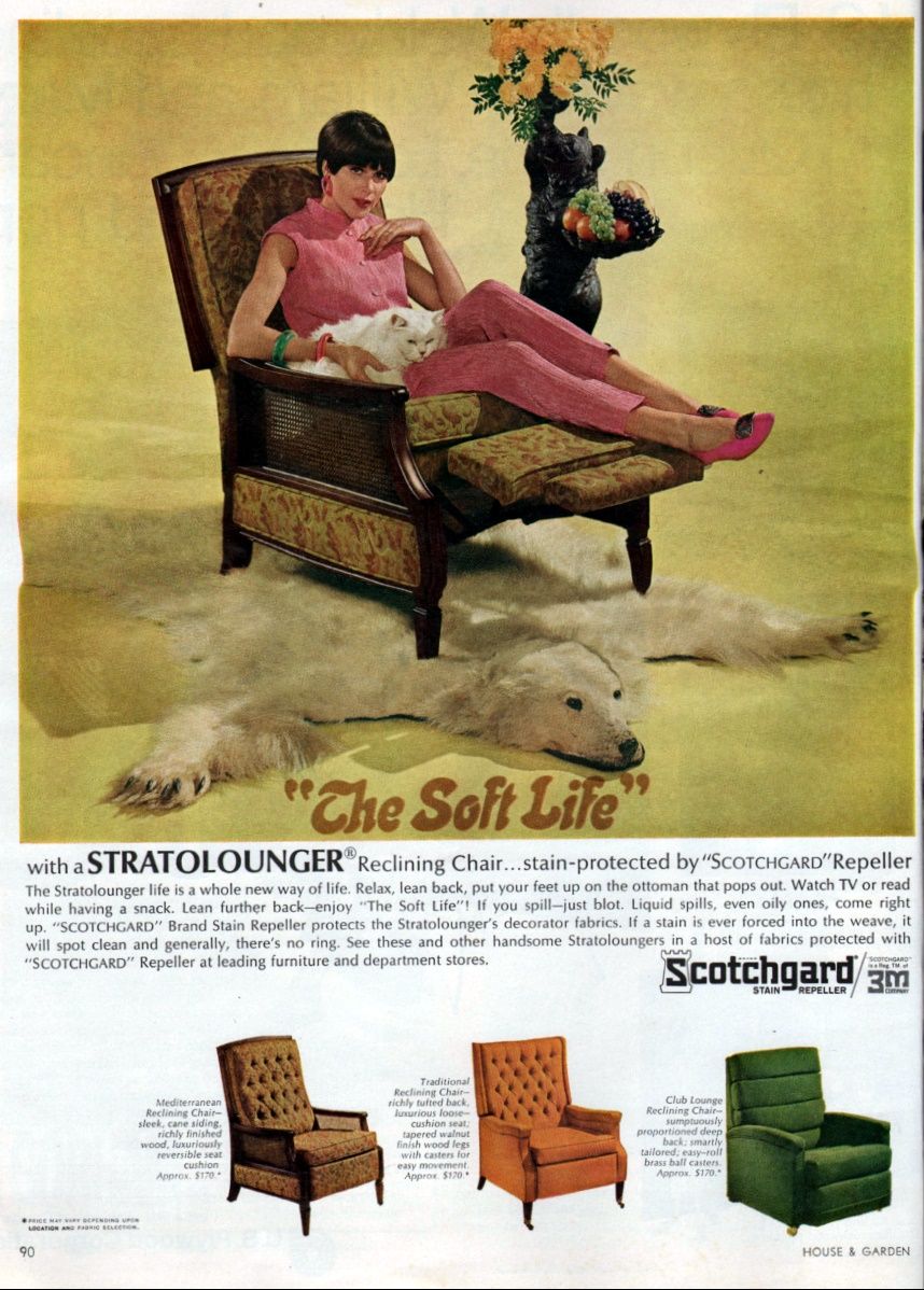 Full-page magazine advertisement for a reclining chair. It shows a woman with short black hair, dressed in comfortable pink clothes, sitting with her legs extended horizontally, supported by the reclining chair. She has a white cat on her lap. Next to her is a small bear-shaped sculpture that holds a bouquet of flowers in a raised paw and a tray of fruit on the other paw. The reclining chair is placed on a rug made of a polar bear skin. The illustration has the text: The Soft Life. Additional text below the illustration says: With a Stratolounger reclining chair... stain-protected by Scotchgard Repeller. The Stratolounger life is a whole new way of life. Relax,lean back, put your feet up on the ottoman that pops out. Watch TV or read while having a snack. Lean further back—enjoy The Soft Life! If you spill—just blot. Liquid spills, even oily ones, come right up. Scotchgard Brand Stain Repeller protects the Stratolounger's decorator fabrics. If a stain is ever forced into the weave, it will spot clean and generally, there's no ring. See these and other handsome Stratoloungers in a host of fabrics protected with Scotchgard Repeller at leading furniture and department stores. Below this text are photographs of three varieties of reclining chair. The first one is light brown. Next to it, the text says: Mediterranean Reclining Chair—sleek, cane sliding, richly finished wood, luxuriously reversible seat cushion. Approximately 170 dollars. There is an asterisk at the end of this text. The second photograph is of a light orange reclining chair. Next to it, the text says: Traditional Reclining Chair—richly tufted back, luxurious loose-cushion seat, tapered walnut finish wood legs with casters for easy movement. Approximately 170 dollars. There is an asterisk at the end of this text. The third photograph is of a dark green reclining chair. Next to it, the text says: Club Lounge Reclining Chair—sumptuously proportioned deep back; smartly tailored; easy-roll brass ball casters. Approximately 170 dollars. There is an asterisk at the end of this text. At the bottom left corner of the illustration is the page number 90 and a note with an asterisk that says: Price may vary depending upon location and fabric selection. At the bottom right corner of the illustration is the magazine title HOUSE AND GARDEN.