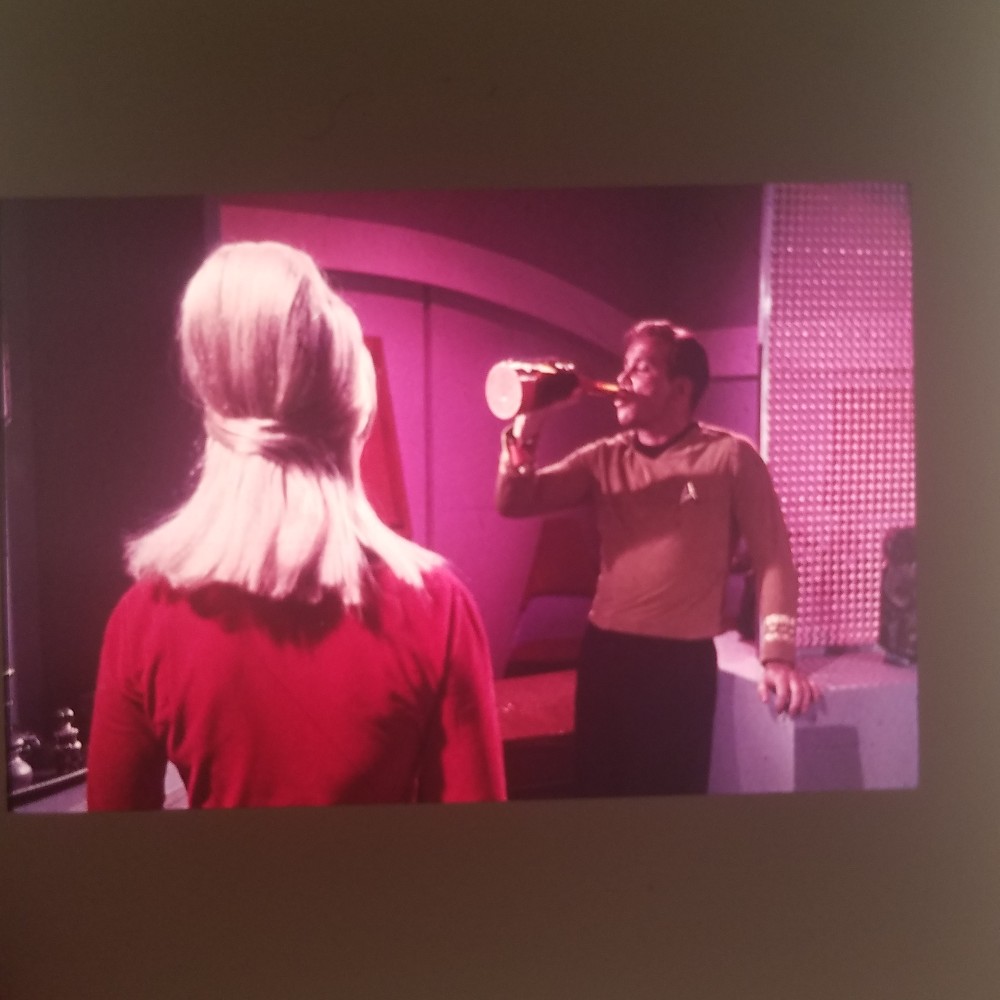 An image projected onto a wall, showing an image from the Star Trek episode 'The Enemy Within', where Kirk is drinking, faced by a Security woman in a beehive hairdo.