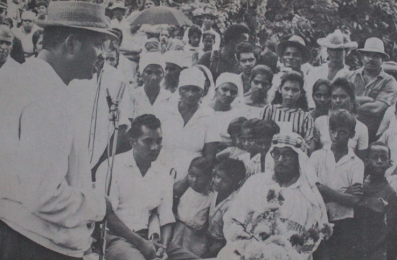 Black-and-white photograph of a Black man speaking in front of an audience outdoors.