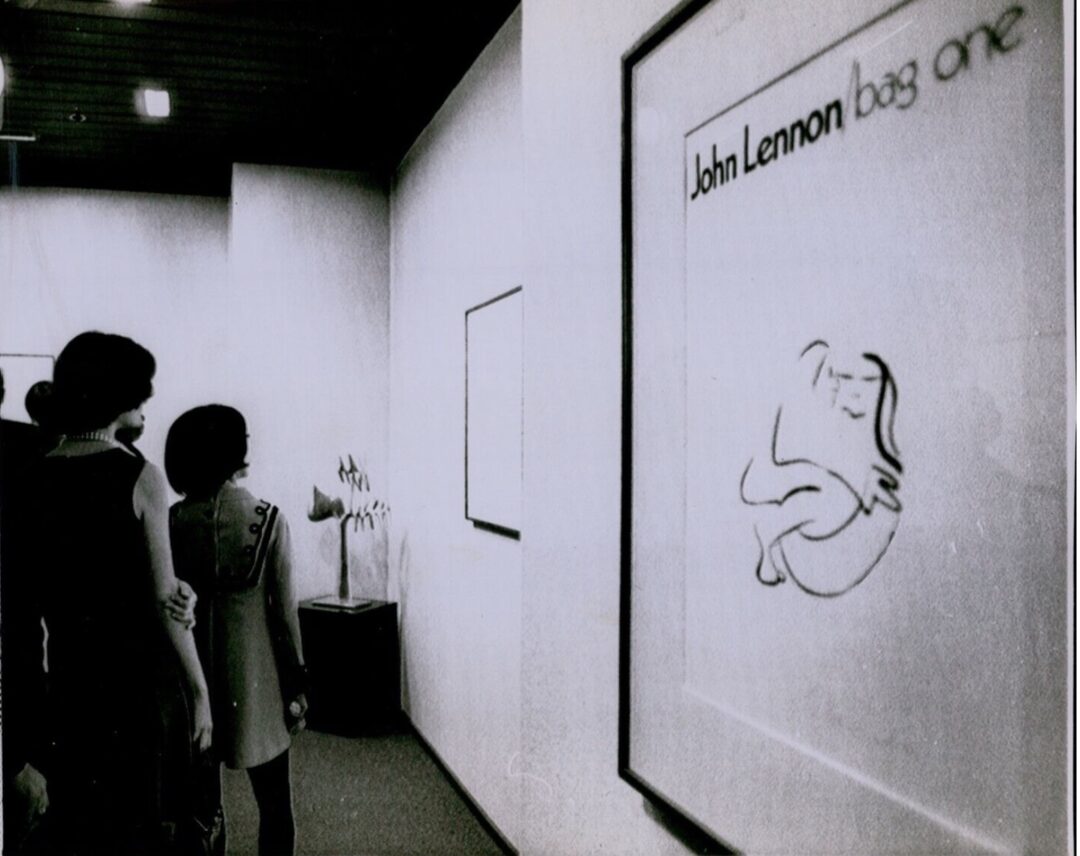 Black-and-white photograph of people standing in front of framed drawings.