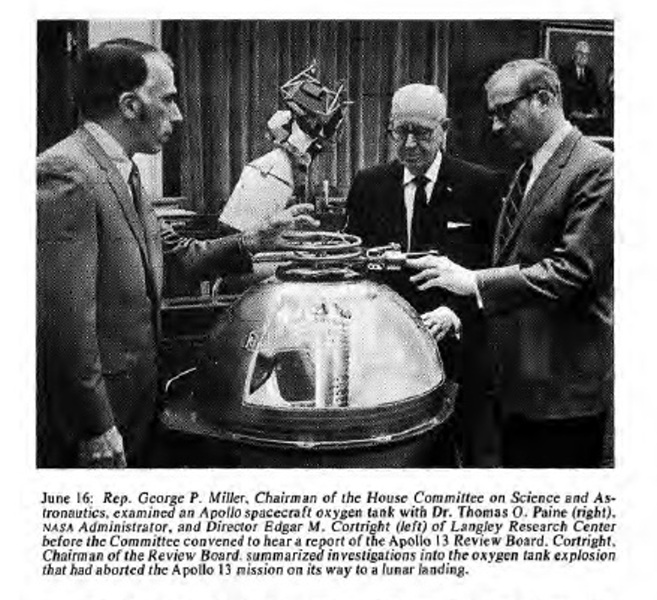 A black and white newspaper clipping.  In front of a large window with drawn curtains, three white men in suits are standing around an oxygen tank from Apollo 13, which is a metallic half-spherical object with a spring on top. The men look down at the tank with serious expressions and gesture toward it with their hands. The caption reads: June 16: Rep George P. Miller, Chairman of the House Committee on Science and Astronautics, examined an Apollo spacecraft oxygen tank with Dr. Thomas O. Paine (right), NASA Administrator, and Director Edgar M. Cortright (left) of Langley Research Center before the Committee convened to hear a report of the Apollo 13 Review Board.  Cortright, Chairman of the Review Board, summarized investigations into the oxygen tank explosion that had aborted the Apollo 13 mission on its way to a lunar landing.