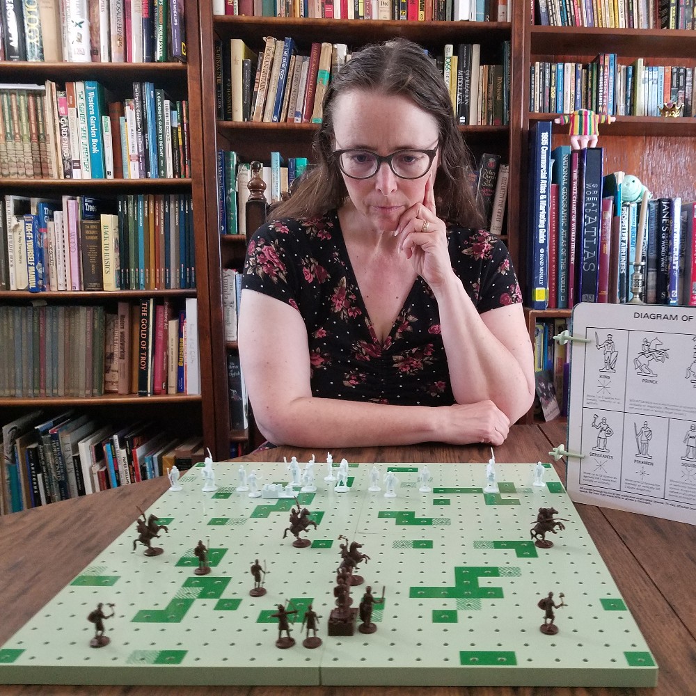 Colour Photograph of a seated white woman looking intently at the game board, pieces all arrayed before her