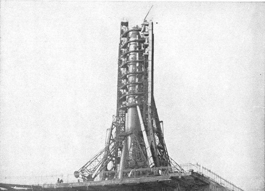 Black & white photograph of a rocket on its launchpad surrounded by a gantry framework