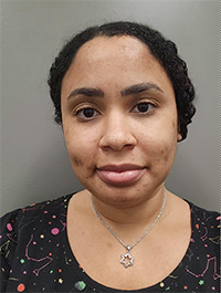 A picture of a young Black woman, wearing an outfit with planetary patterns, as well as a silver necklace.