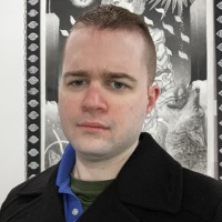 A young white man with short hair wearing a navy P-coat, blue polo collar, and green t-shirt.