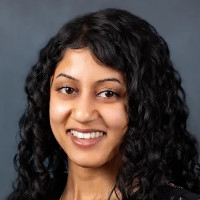 A photo portrait of Winona Mendezes. She is a woman with light-brown skin, long black curly hair and dark eyes. She is smiling at the camera.