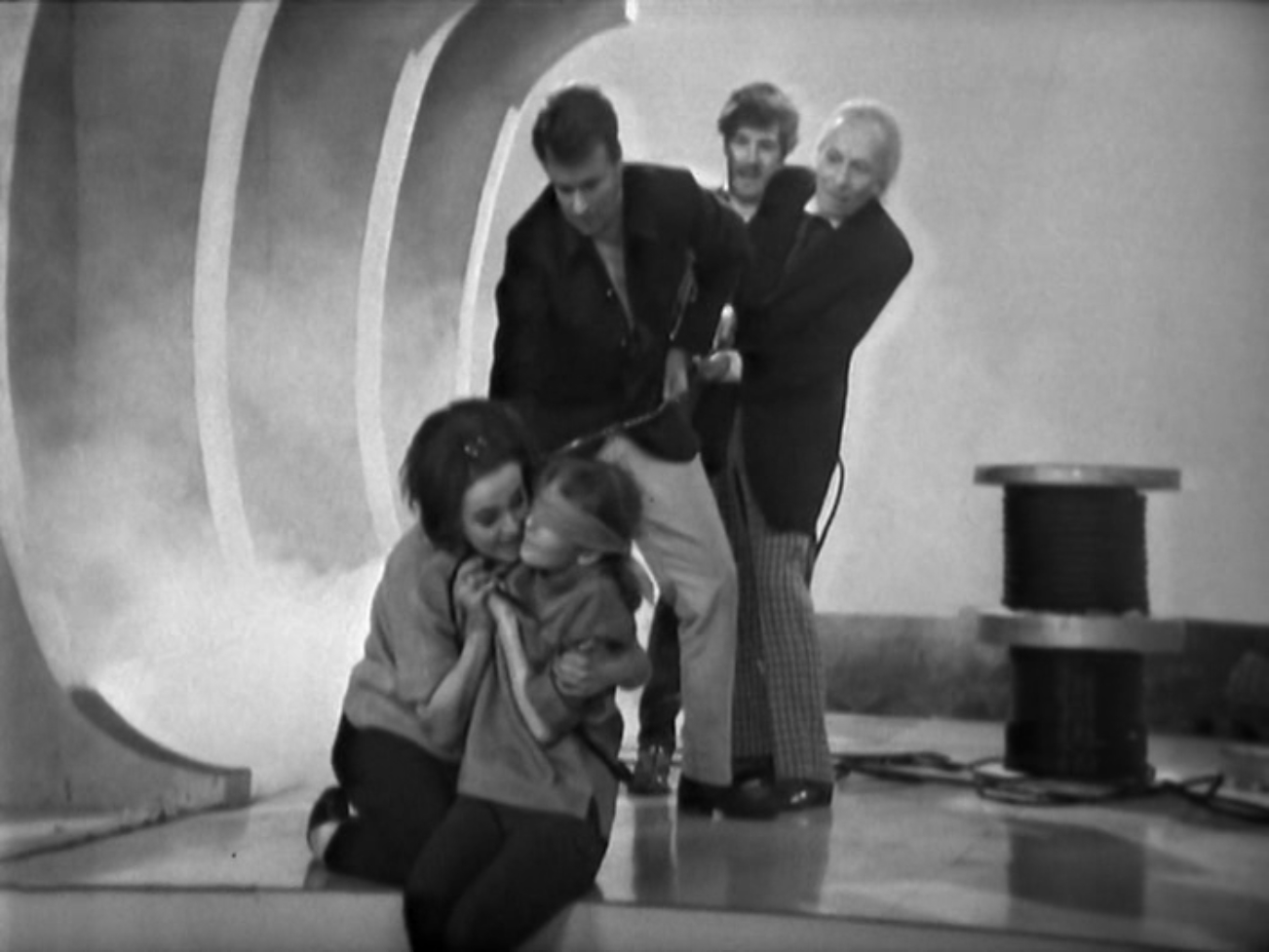 Image description: Barbara, Ian, the Doctor and Steven hold onto a rope that is tied around Vicki's waist. Vicki is blindfolded.