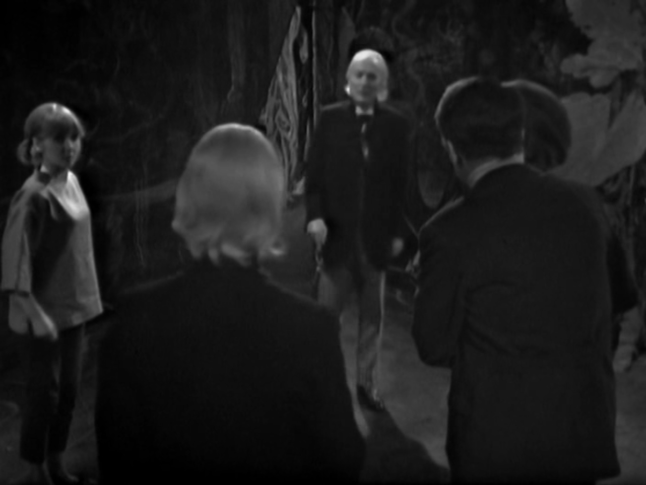 Image description: In the foreground is the Doctor with his back to the camera. Vicki, Ian and Barbara are in the midground. There is another Doctor in the background facing the first Doctor.