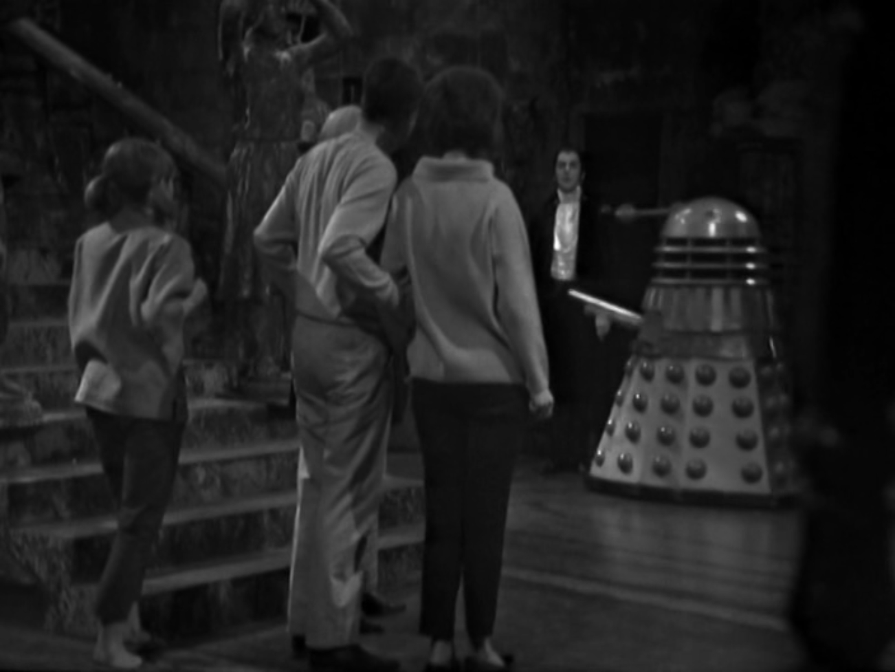 Image description: In the foreground with their backs to the camera are Vicki, Ian and Barbara, with the Doctor partially visible. In the background are Dracula and a Dalek.