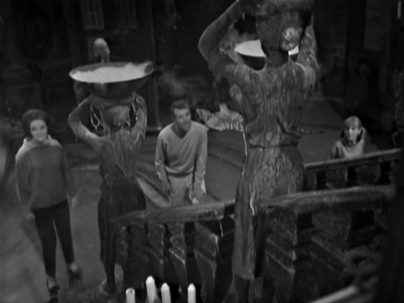 Image description: In the foreground there is a staircase with smoking braziers. In the midground are Barbara, Ian and Vicki. The Doctor is in the background.