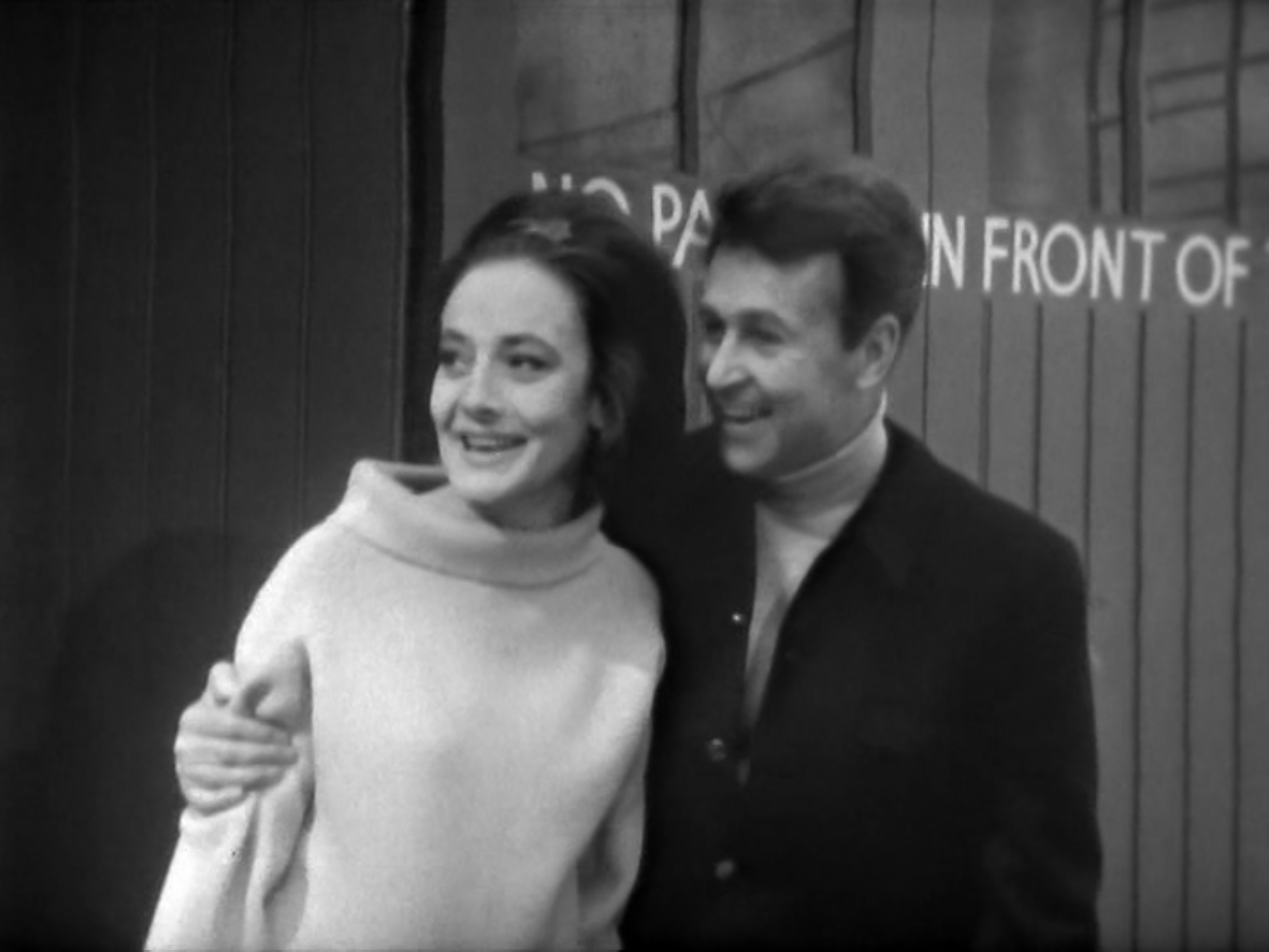 Image description: Ian with his arm around Barbara in front of a 'No Parking' sign. Both appear very happy.