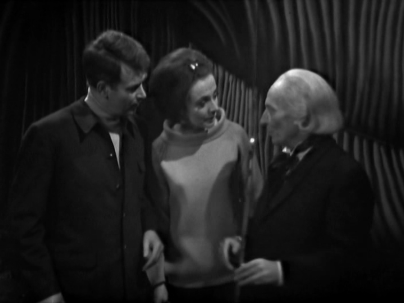 Image description: Ian and Barbara look at the Doctor as he shows them a lit wand.