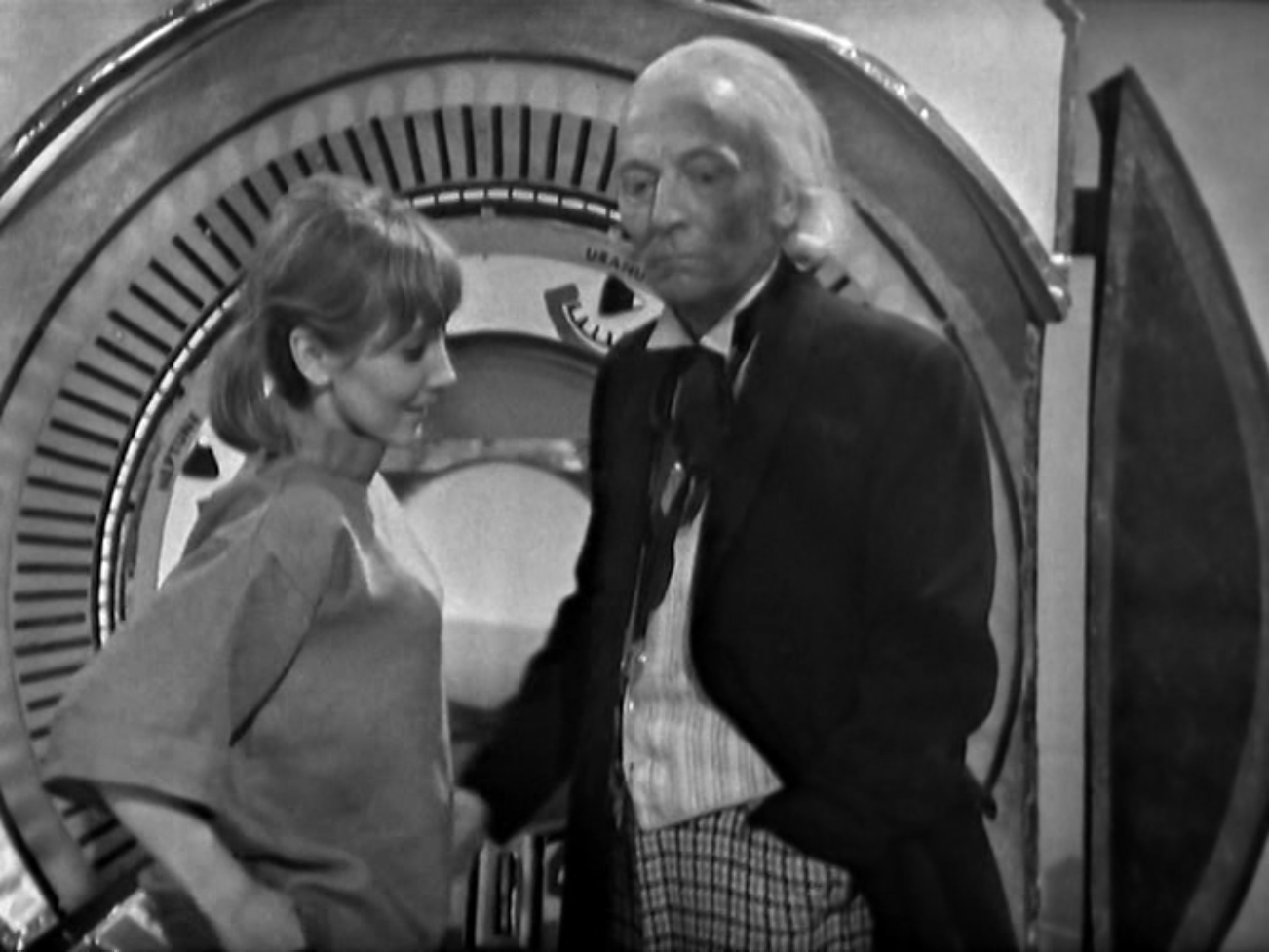 Image description: Vicki and the Doctor stand in front of the Time And Space Visualiser. Vicki is smiling, but the Doctor appears morose.