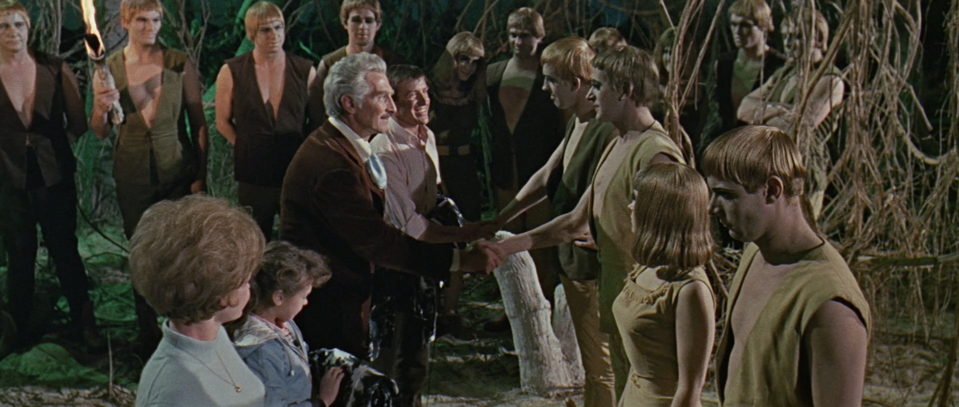 Image description: In the foreground, the four main cast members shake hands with a number of Thals. There are more Thals in the background.