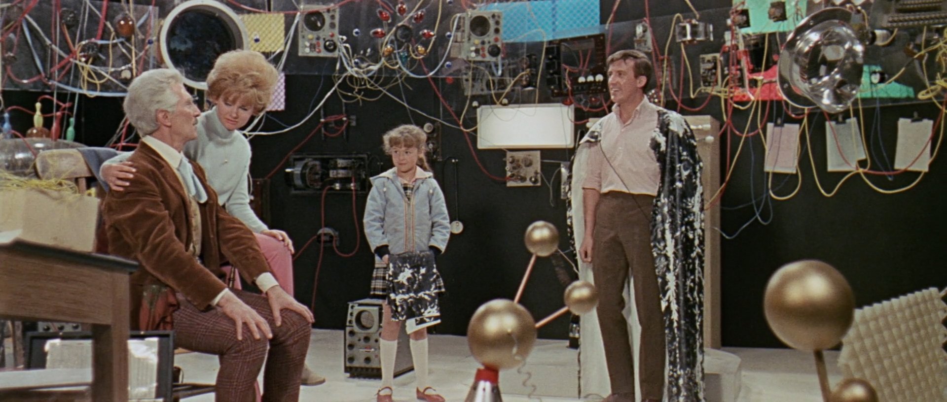 Image description: Dr. Who, Barbara, Susan and Ian inside TARDIS. There are many wires hanging down and a lot of scientific equipment.