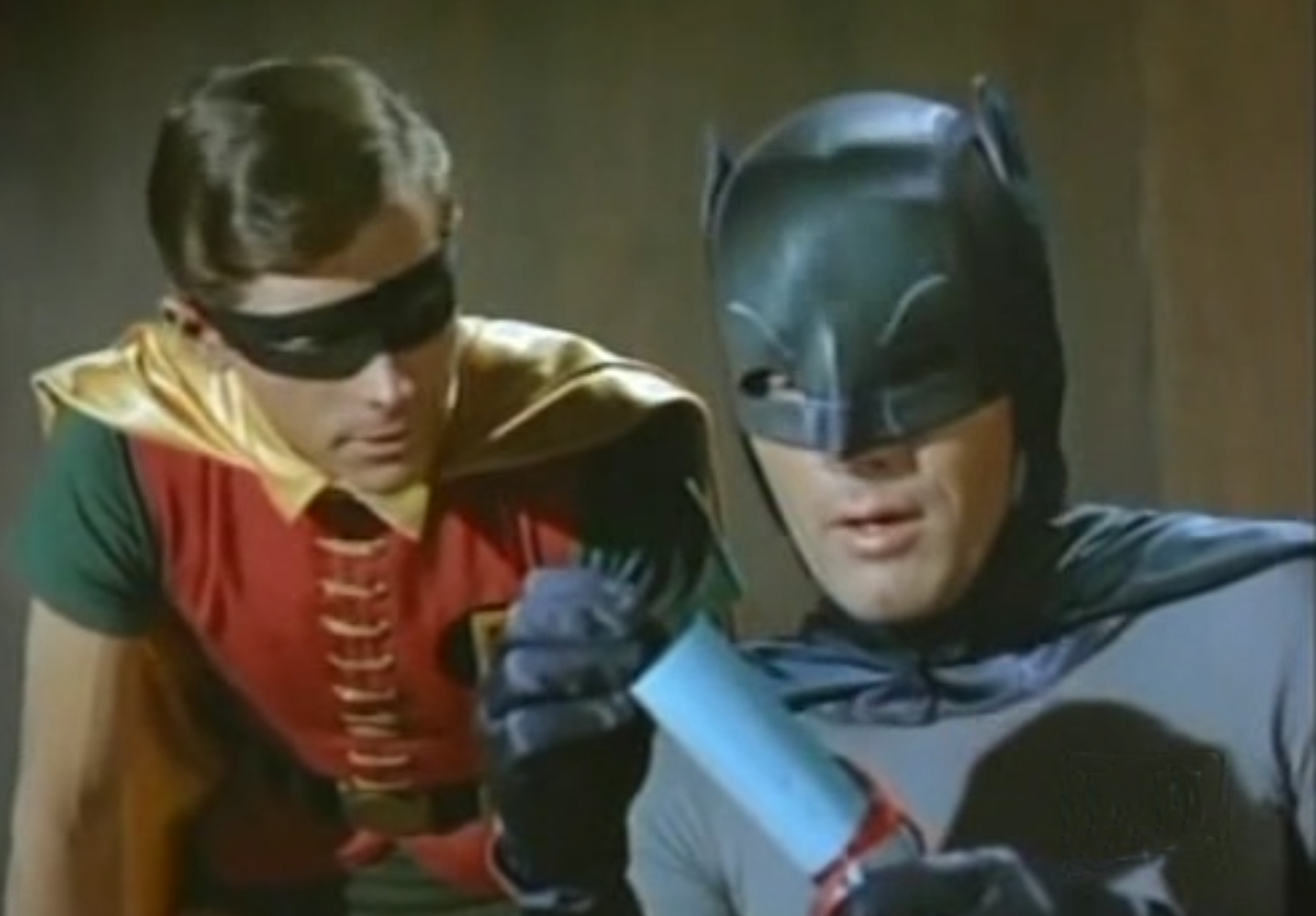 Batman holding a scroll, Robin standing over his shoulder