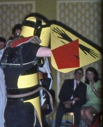 A person wearing a home-made knight costume with black and yellow 'armour'. Onlookers appear amused.