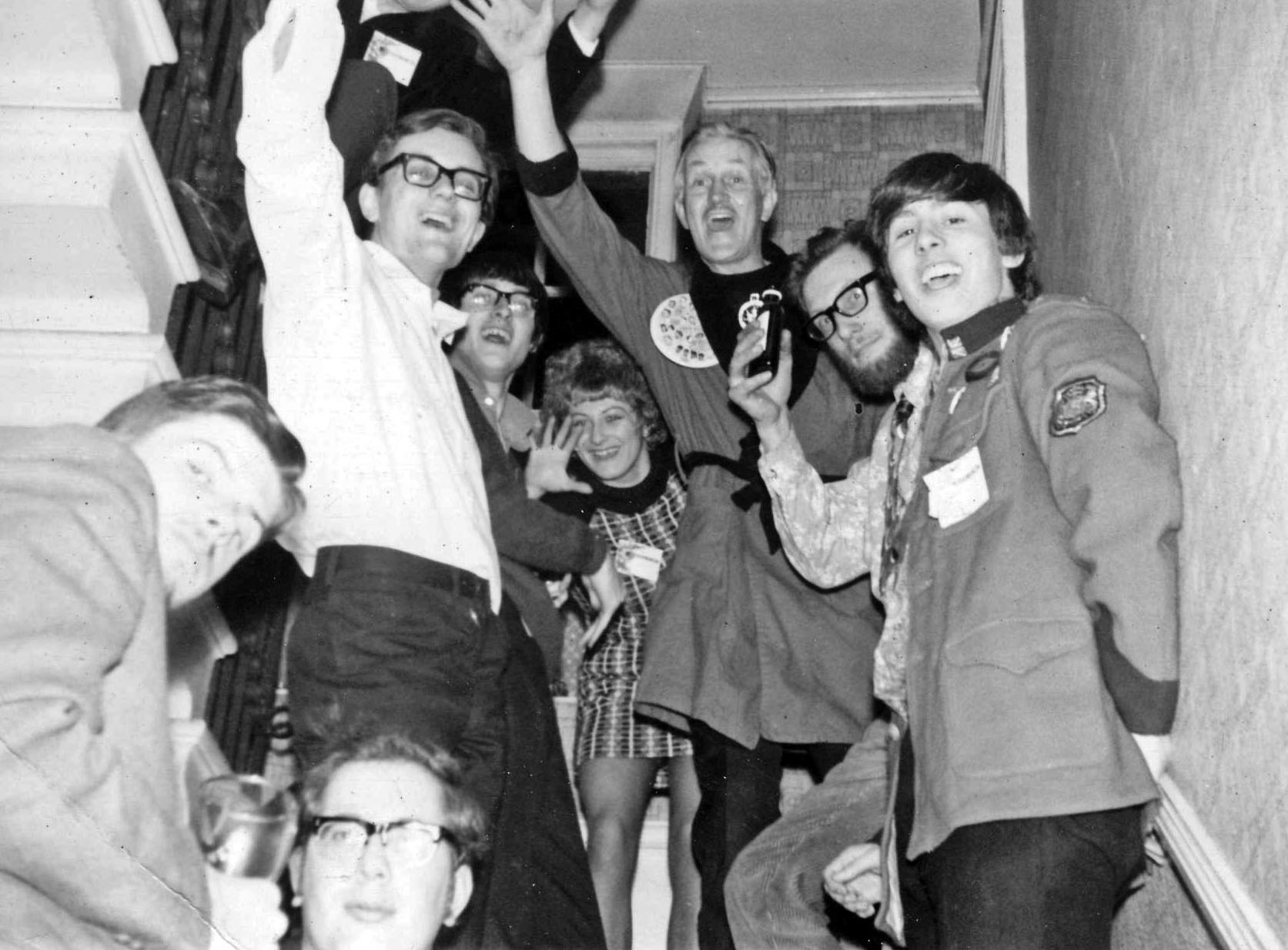 A group of science fiction fans, some in costume, standing cheering and drinking on a stairwell.