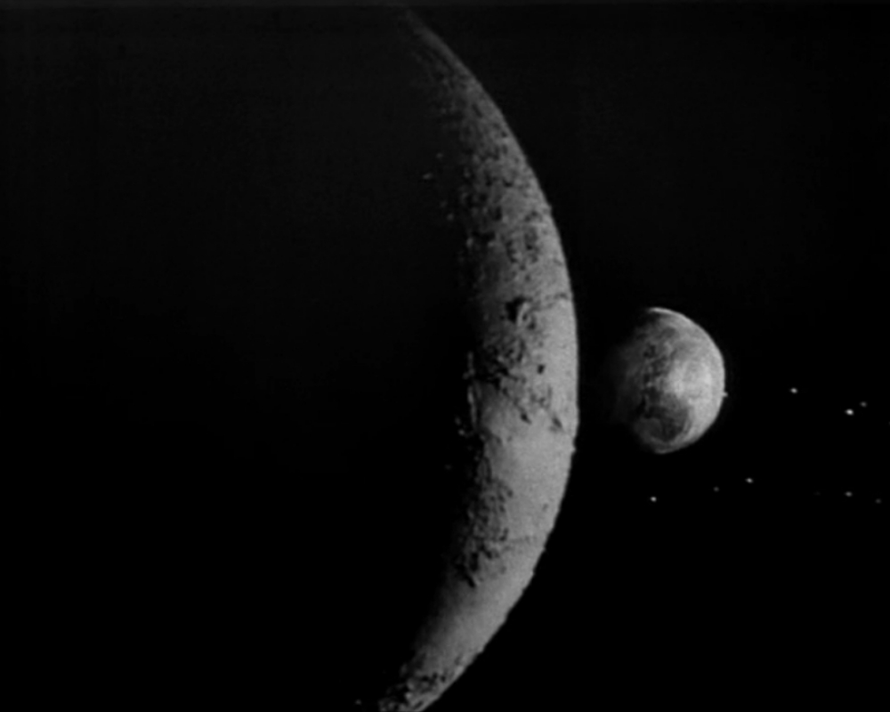 ID: The Moon and Earth as seen from orbit. The Moon is only lit along the edge, and is in the foreground. Earth is half-lit, in the background.