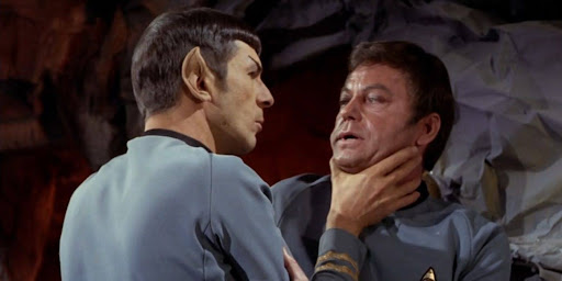 Spock has his palm wrapped around McCoy's neck, the doctor pressed against the cave wall