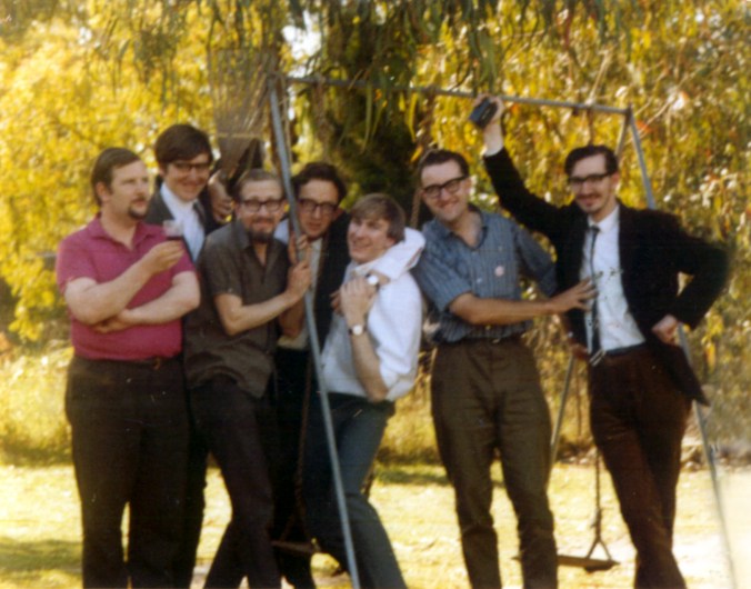 a light-hearted photo of seven young men standing by a swing set