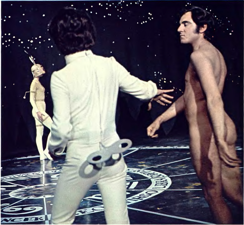 A nude man walks on a dance painted with a zodiac; two clockwork men are also on the floor.