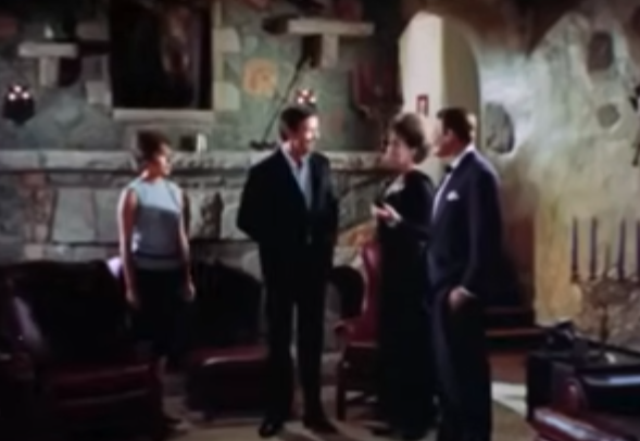 A still from Blood of Dracula's Castle depicting four people chatting in the hall of a castle.