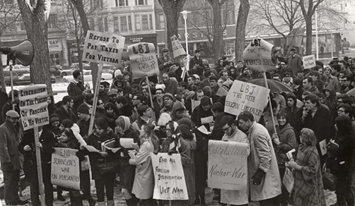 Black and White photo of a protest by Students For A Democratic Society, holding up signs saying:
"Refuse to pay taxes for Vietnam"
"Liberalism in the pursuit of fascism is no virtue"
"End Johnson's war on peasantry"
"LBJ, the lesser Evil?"
"End All Foreign Intervention in Vietnam"
"LBJ: The Myth of American Liberalism"
"Escalation Means Nuclear War"