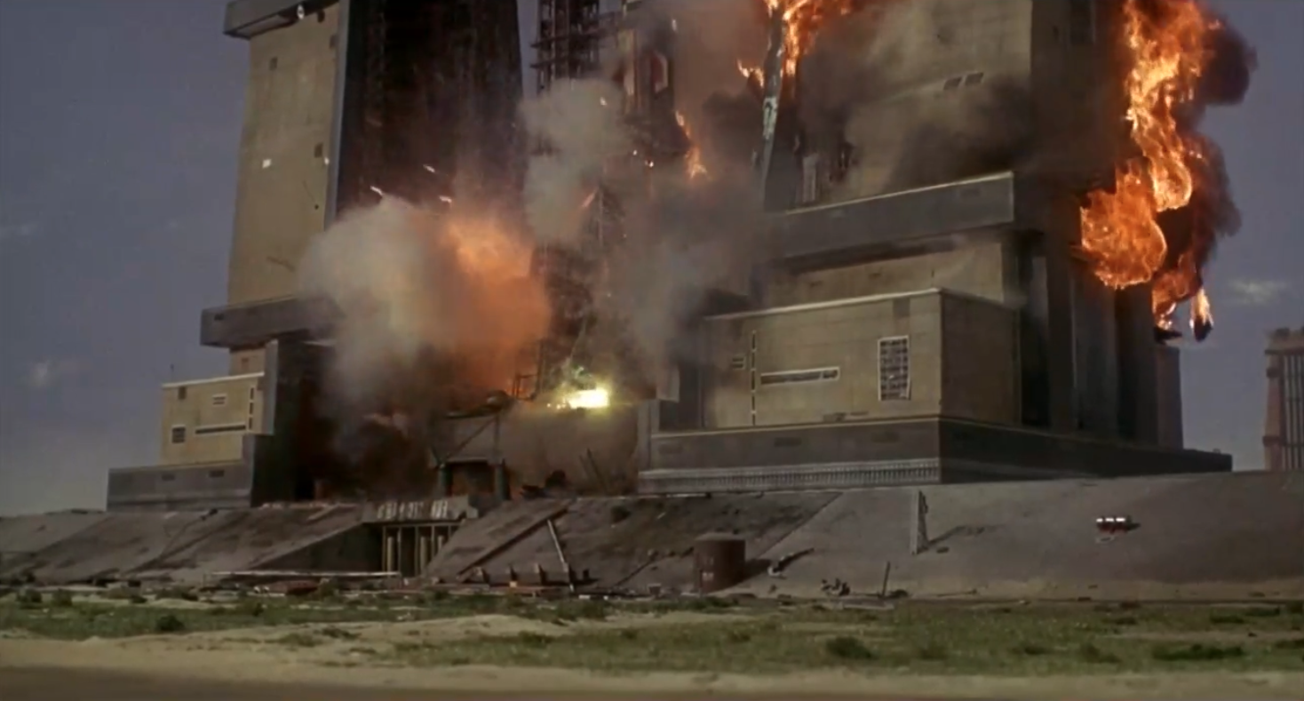 A photo of a scene. The huge Eurosec building is seen exploding on screen. There is a huge amount of smoke and flames.