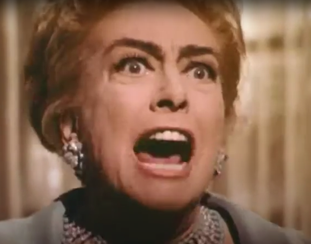 Still frame from the TV series Night Gallery. It shows a close-up of a white, red-haired, middle-aged Joan Crawford wearing elegant jewels and screaming in anger.