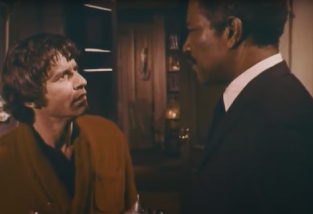 Still frame from the TV series Night Gallery. It shows the character Portifoy talking to a white man in a red smoking jacket.