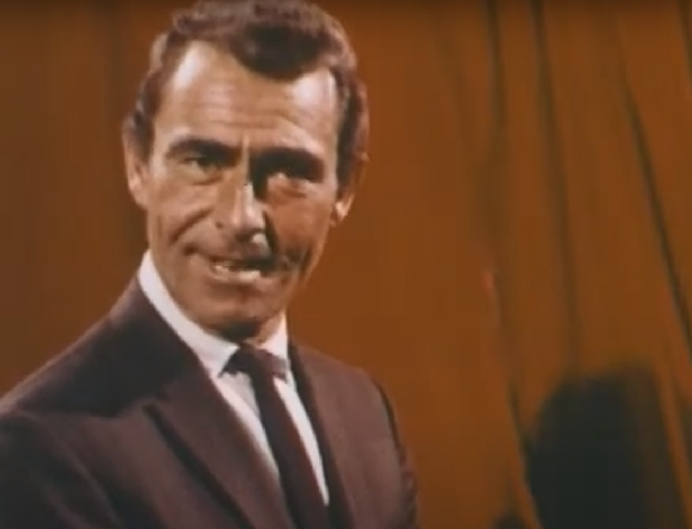 Still frame from the TV series Night Gallery. It shows Rod Serling in a suit and tie, talking to the camera. There is a red curtain behind him.