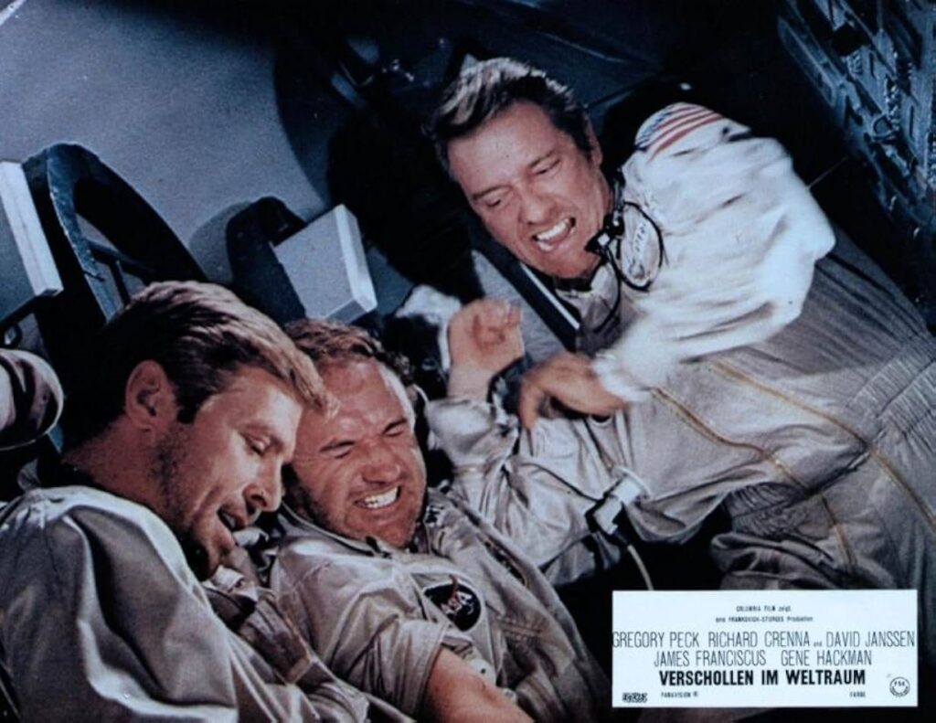 German promotional picture for the movie. There are three characters in spacesuits in a tiny space. One seems tense, one excited and one focused.