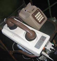 Photograph of a push-button landline telephone with its handset placed atop another device, which is connected to computer cables.