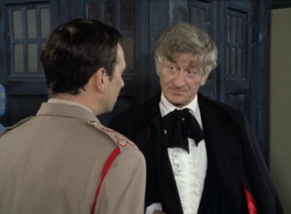 The Brigadier and the Doctor in front of the TARDIS. The Brigadier has his back to the camera and is talking to the Doctor, who has a sardonic expression. 