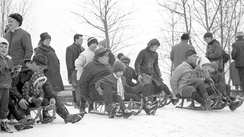 Adults and children are frolicking in the snow on wooden sleds