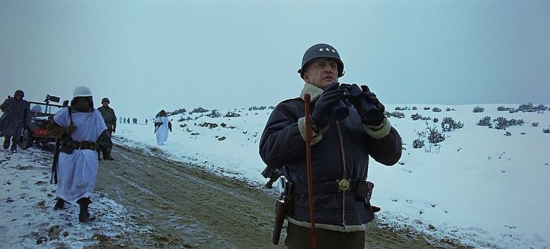 Patton standing in the snow with his binoculars, infantry behind him