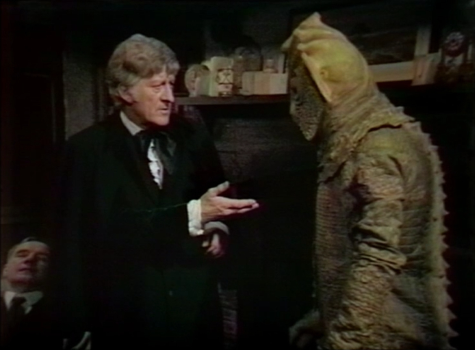 The Doctor offers a hand to a Silurian. The Silurian is a little taller than him and has green scaly skin.