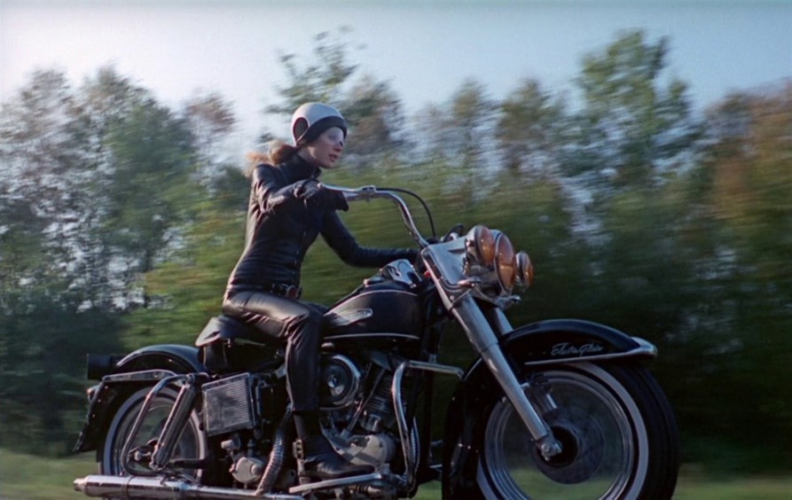 Shot from Girl on a Motorcycle of Marianne Faithful riding along a forested road on a motorcycle.