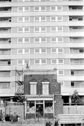 Reconstruction taking place in the Isle of Dogs as a Victorian building is being demolished in the foreground and a high rise flat complex rises behind it.