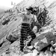 Scene from the film Fugitive From A Chain Gang showing a line of men in chained together breaking rocks in a quarry.