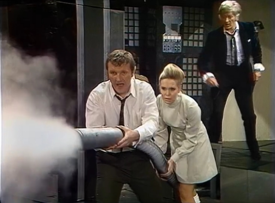 Sutton and Petra aim a long hose spewing white smoke, as the Doctor looks on behind them.