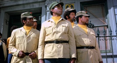 Picture of a quartet of Black men standing at alert and looking to their left, all wearing outfits suggestive of military uniforms